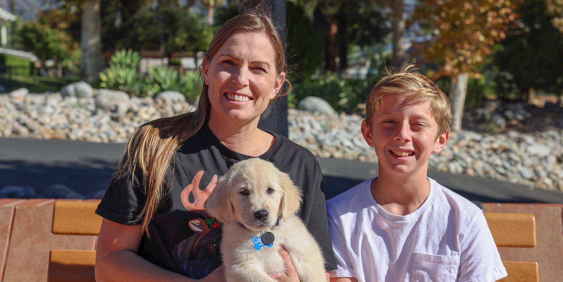 mother and son smile on bench with young puppy